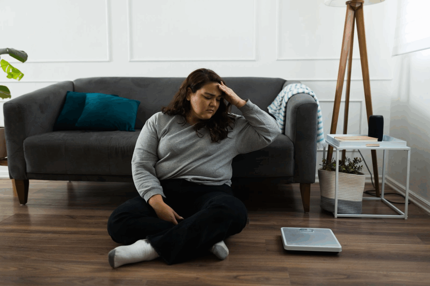 Woman seated, contemplating scales on floor.